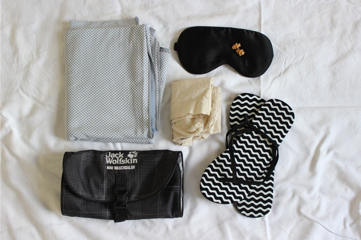 Reisehandtuch, Kosmetikbeutel mit Haken, Badeschlappen, eine Tüte für Klamotten, Schlafmaske und Ohrstöpsel