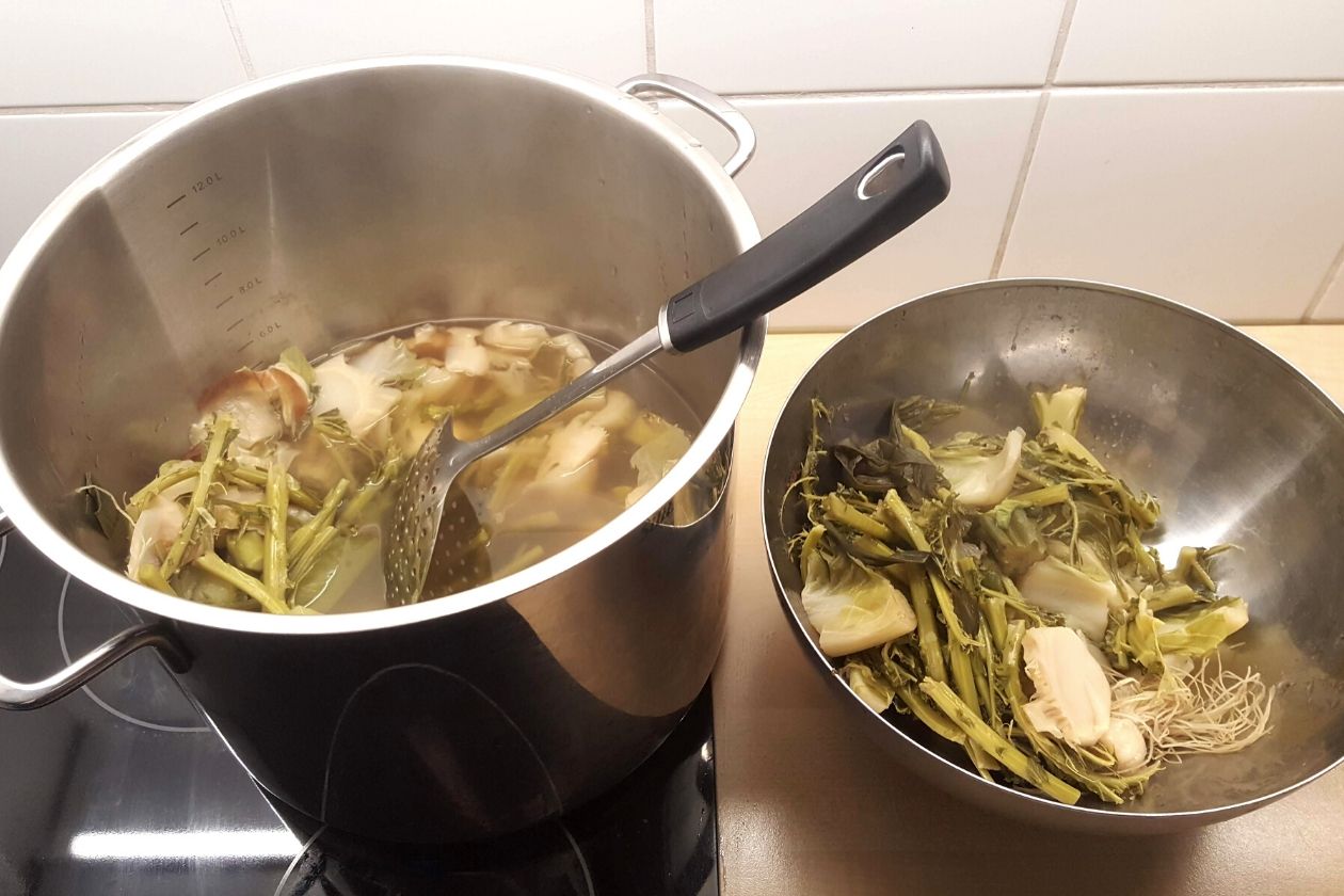 Der Topf mit der gekochten Zero Waste Gemüsebrühe mit einer Schaumkelle darin. Daneben der Abfallbehälter.