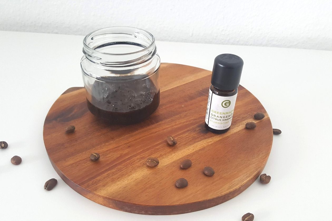 Das Zero Waste Kaffee-Orangen Peeling in einem Schraubglas und das Orangenöl daneben, beides plaziert auf einem Brett. Kaffebohnen liegen drum herum.
