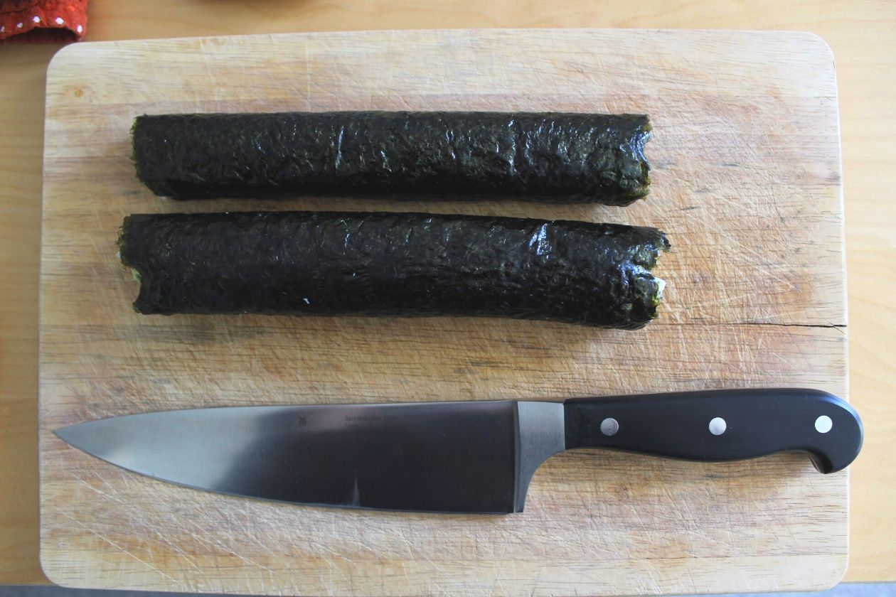 Die fertigen Sushi-Rollen auf einem Brett. Darunter liegt ein Messer.